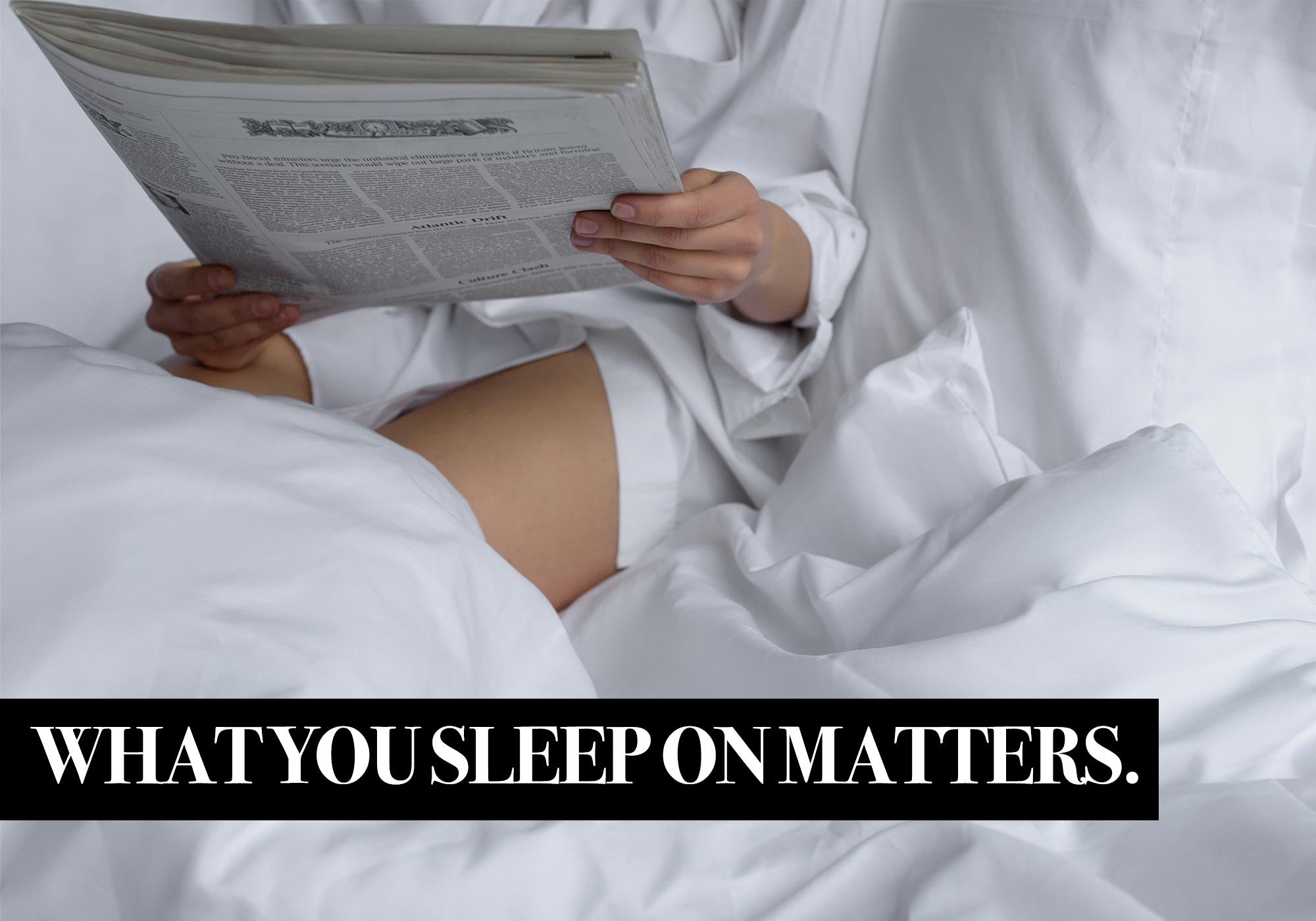 Woman sitting in bed with a silk pillowcase and duvet, reading a newspaper.