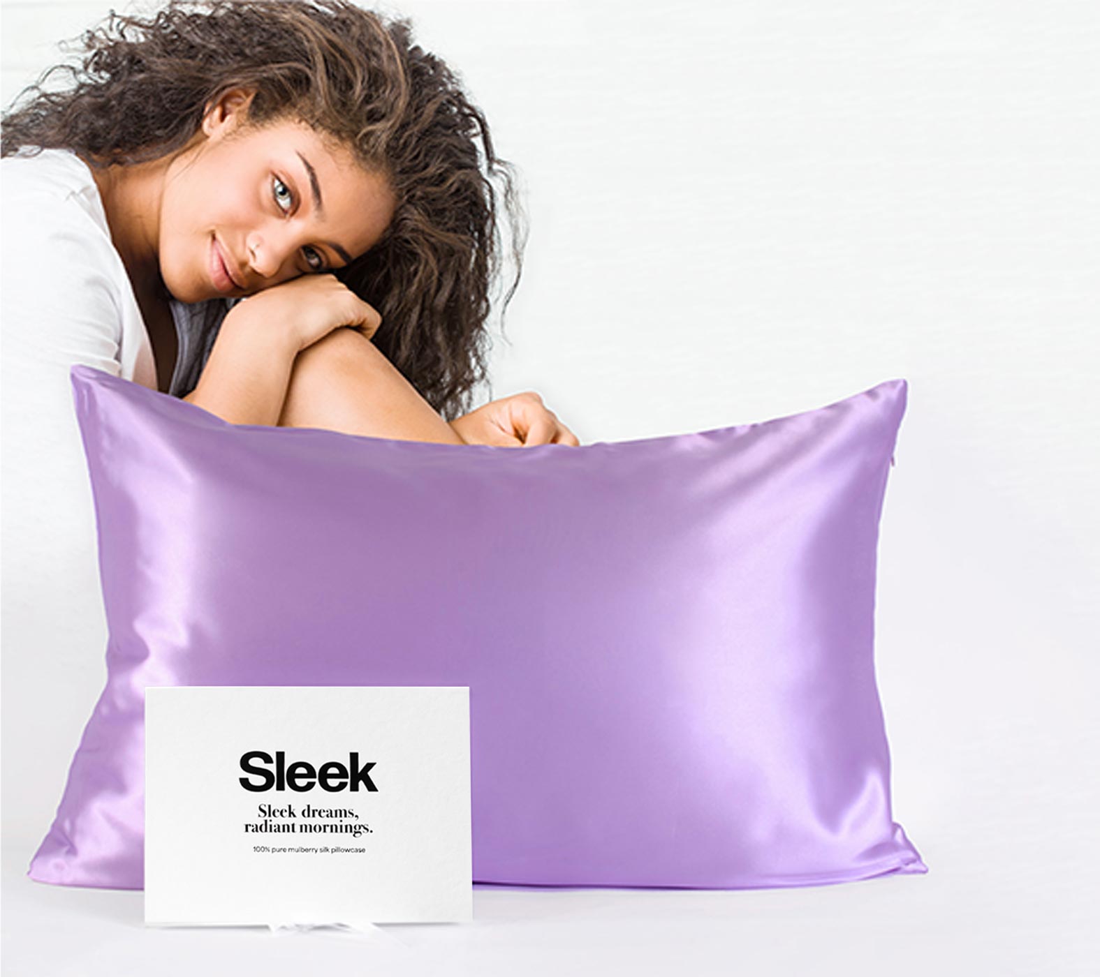 Brunette girl sitting behind a silk pillowcase and gift box, suggesting she will use the pillowcase to improve her wavy hair.